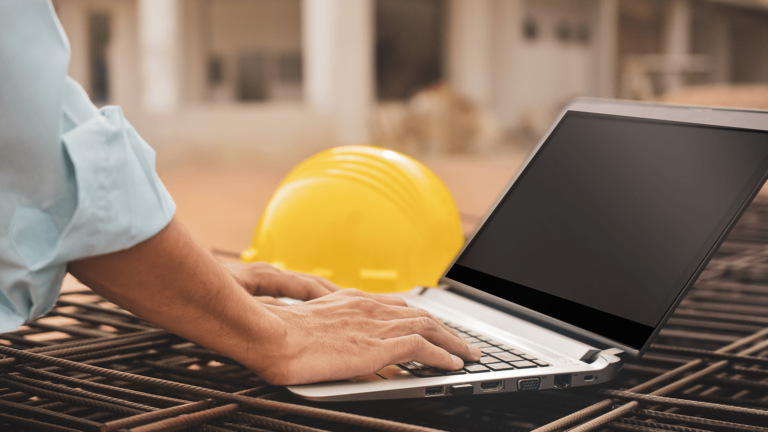 person-typing-on-laptop-next-to-hardhat-at-a-construction-site